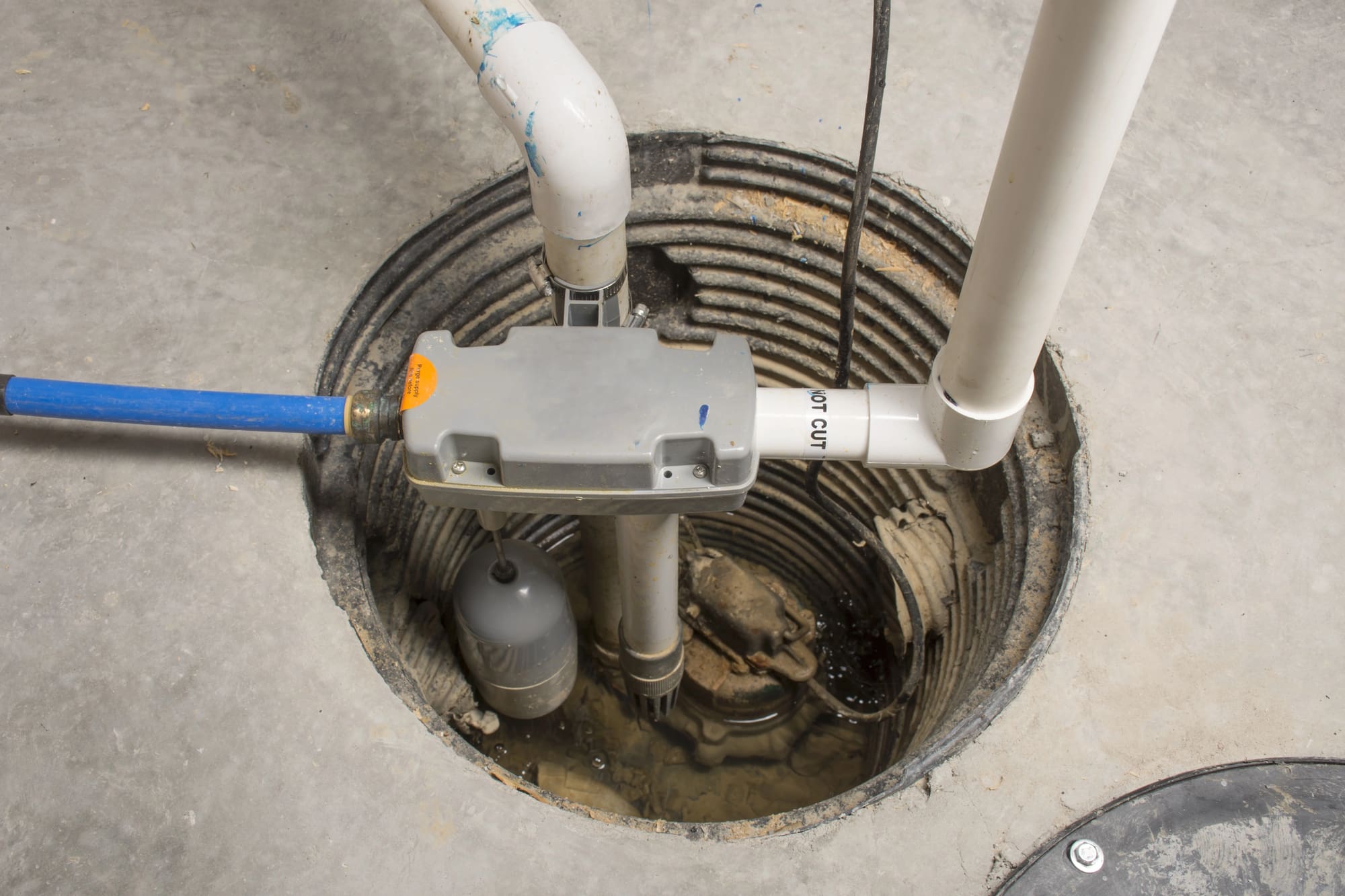 Sump pump installation San Francisco: closeup of pump system with drainage pipes in concrete basin